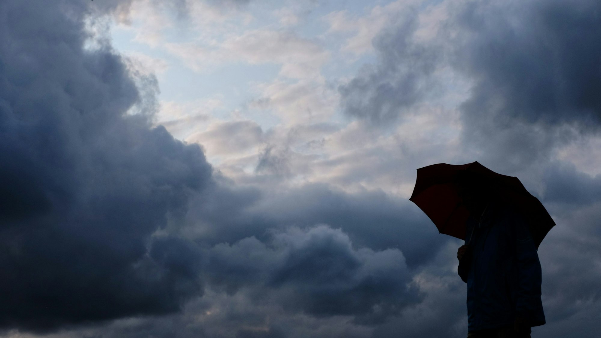 Ein Mann geht mit einem Regenschirm vor aufziehenden dunklen Wolken spazieren.