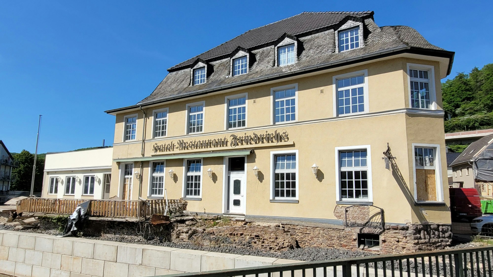Das Foto zeigt das markante Hotel am Ufer der Urft, vor deren Wasser es durch eine Wand aus Betonsteinen geschützt wird.