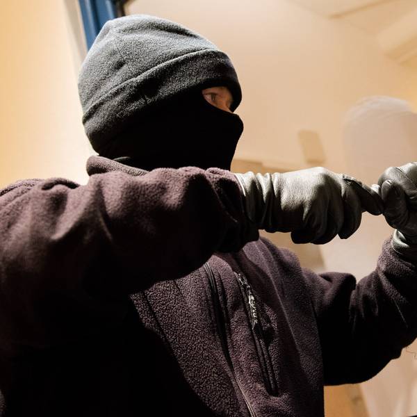 Ein vermummter Einbrecher hebelt ein Fenster auf.