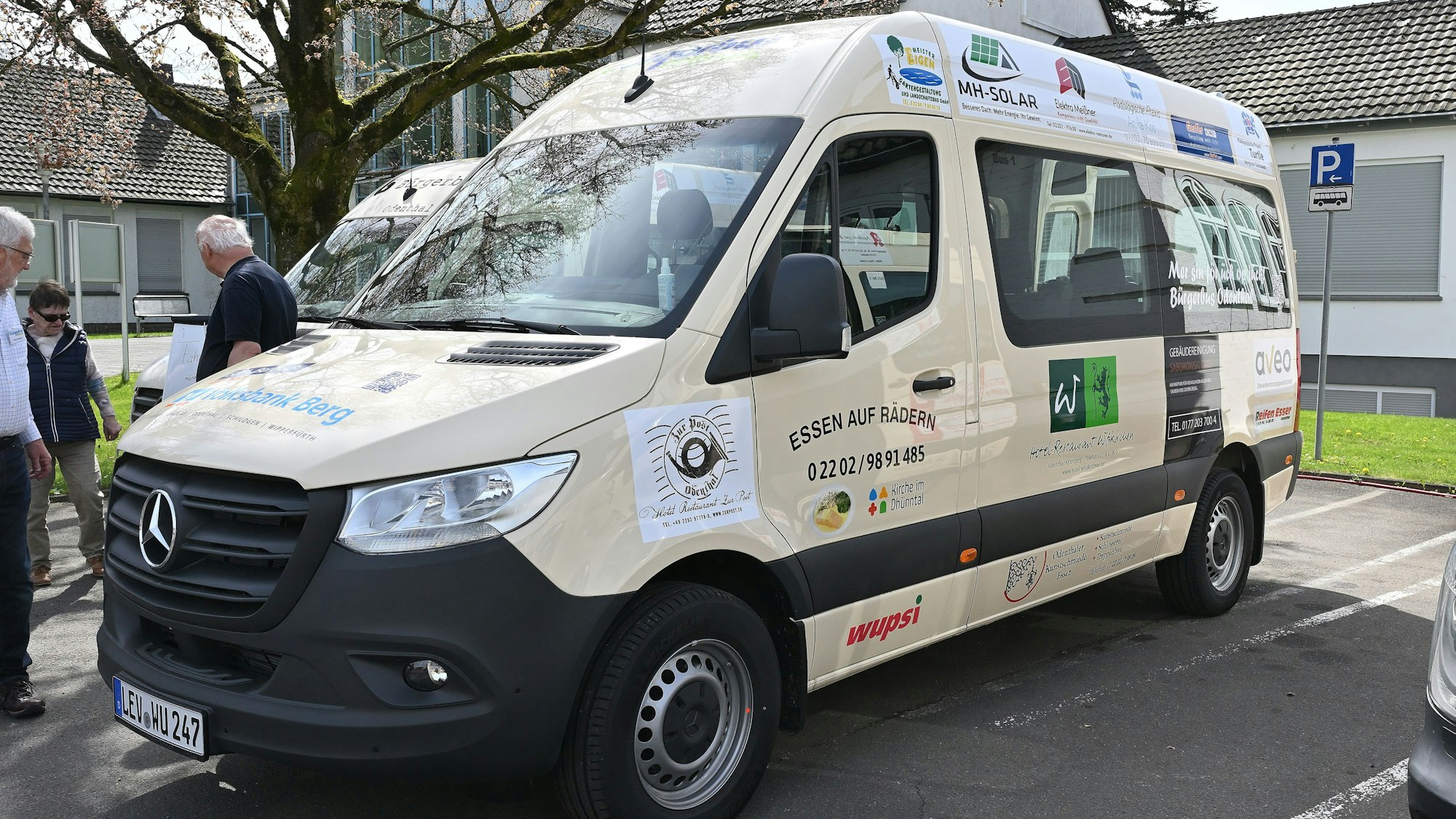 Ein weißer Kleinbus mit Werbebeschriftung steht auf einem Parkplatz.