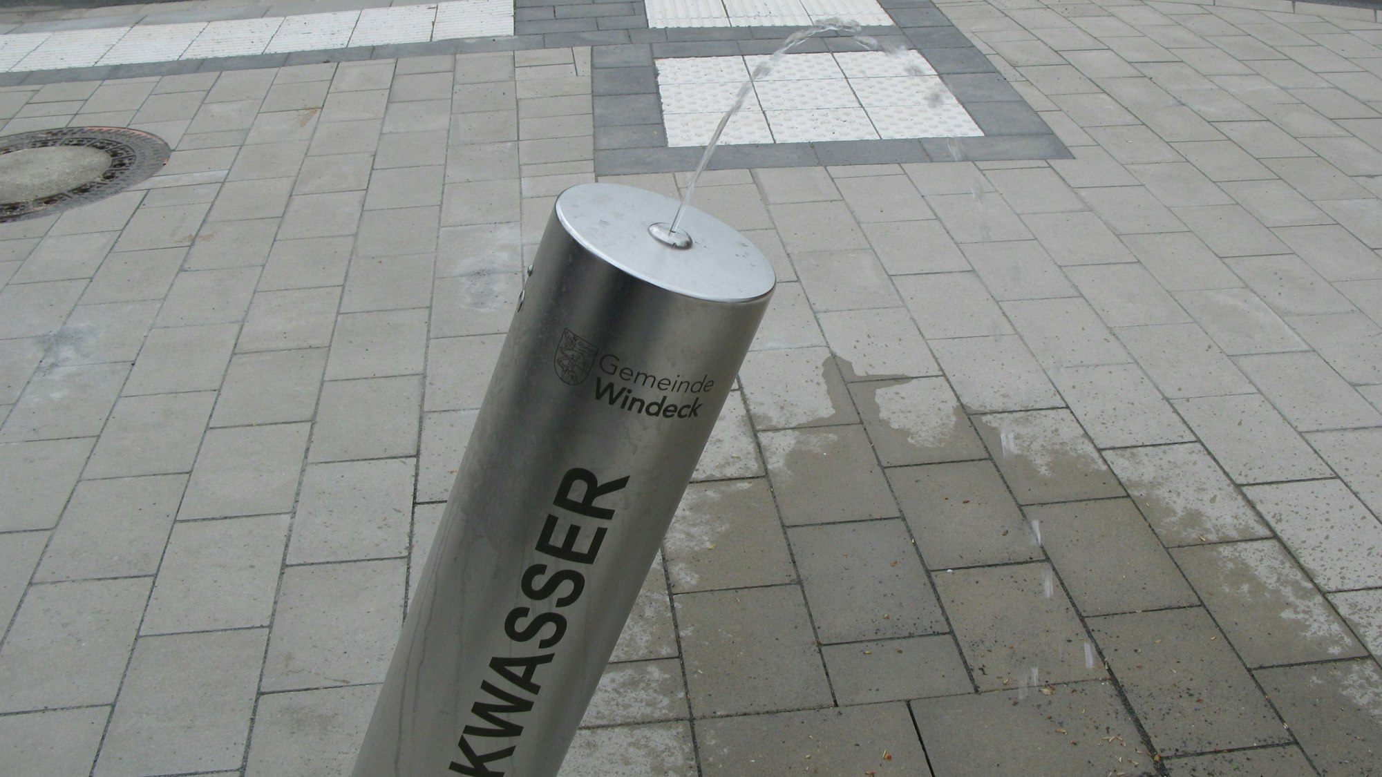Aus einer schräg stehenden Stahlsäule kommt ein Trinkwasserstrahl.