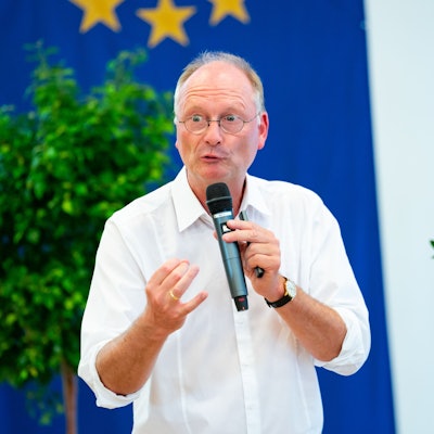 Wetterexperte und Meteorologe Sven Plöger hält bei einem Vortrag ein Mikrofon in der Hand. Er trägt ein weißes Hemd und eine Uhr.