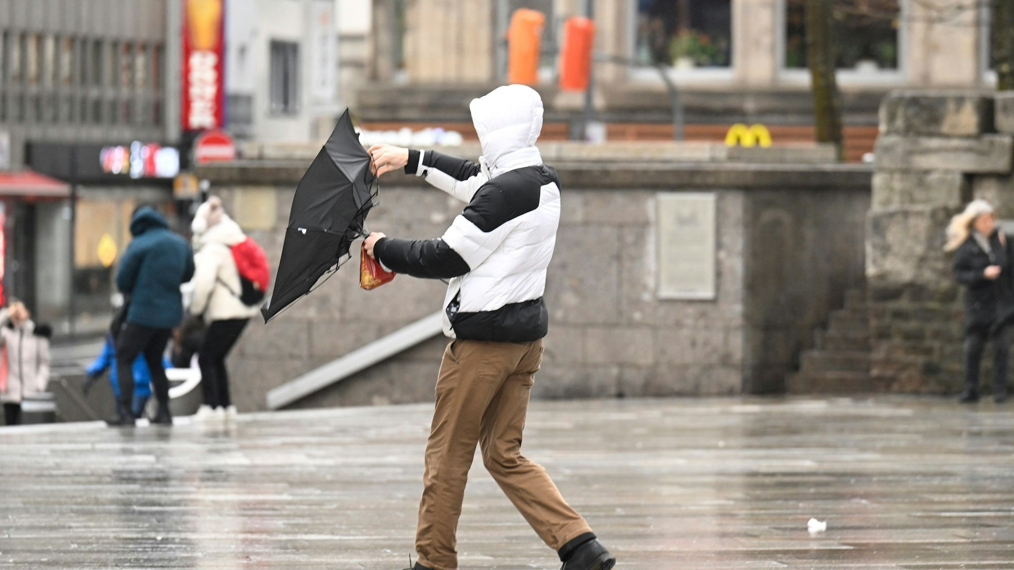 Köln: Ein Mann kämpft bei stürmischem Wetter mit seinem Regenschirm.
