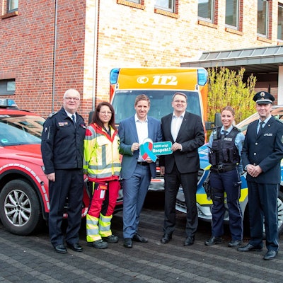 Alexander Rheindorf, Jessica Jeub, Markus Ramers, Udo Becker, Christina Specht und Wolfgang Henseler haben sich zum Gruppenfoto aufgestellt, flankiert von Fahrzeugen der Feuerwehr, des Rettungsdienstes und der Polizei. Ramers und Becker halten ein Respekt-Schild hoch.