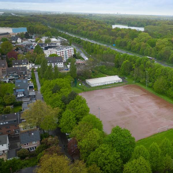 Das Luftbild zeigt einen Aschenplatz inmitten von Grün zwischen Autobahn und Wohnbebauung.