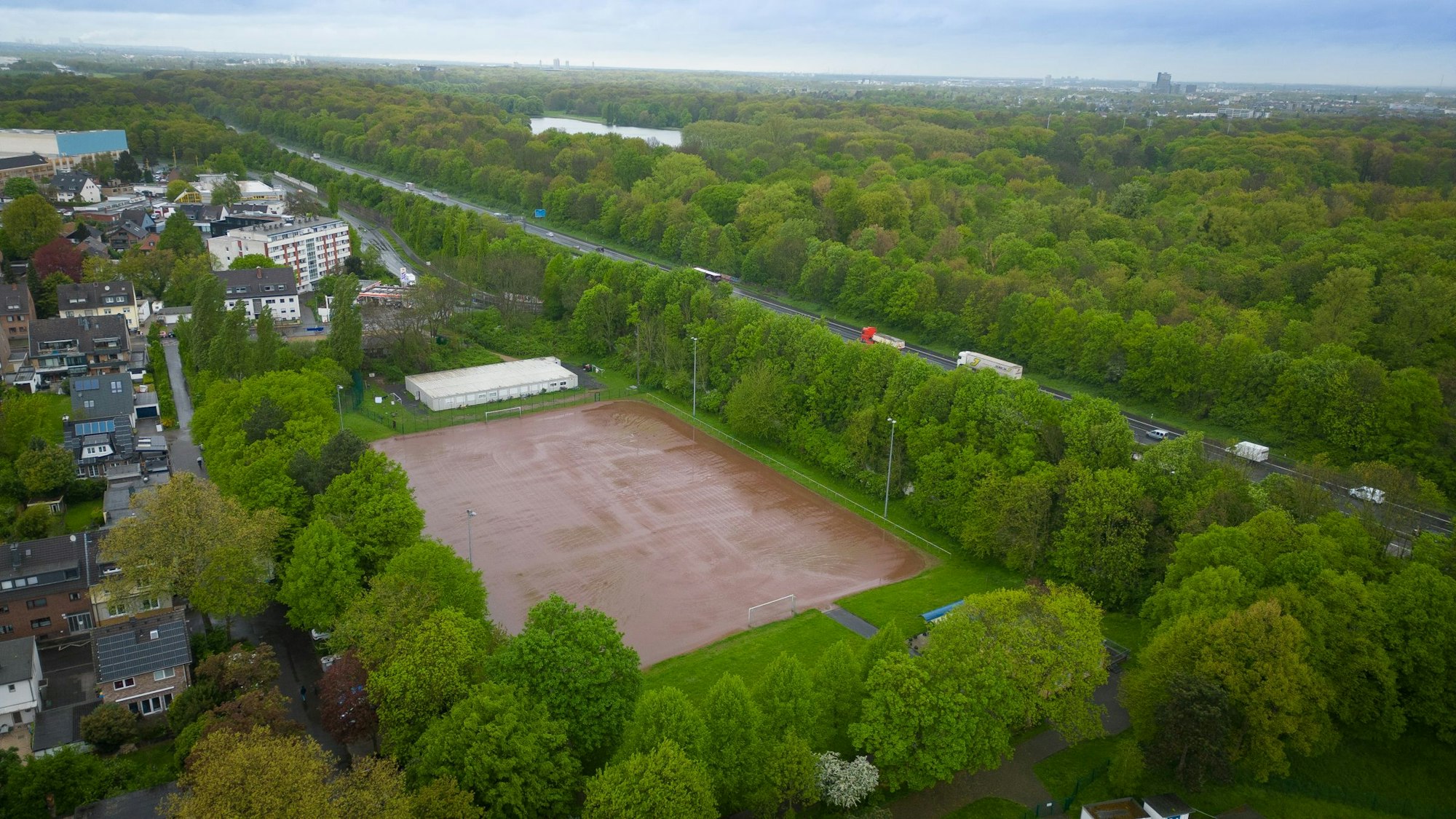 Das Luftbild zeigt einen Aschenplatz inmitten von Grün zwischen Autobahn und Wohnbebauung.