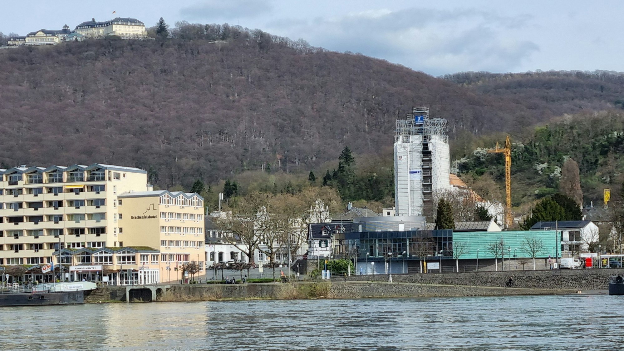 Die Ansicht der Stadt Königswinter vom Rhein aus, im Zentrum die eingerüstete Pfarrkirche St. Remigius, im Hintergrund der Petersberg