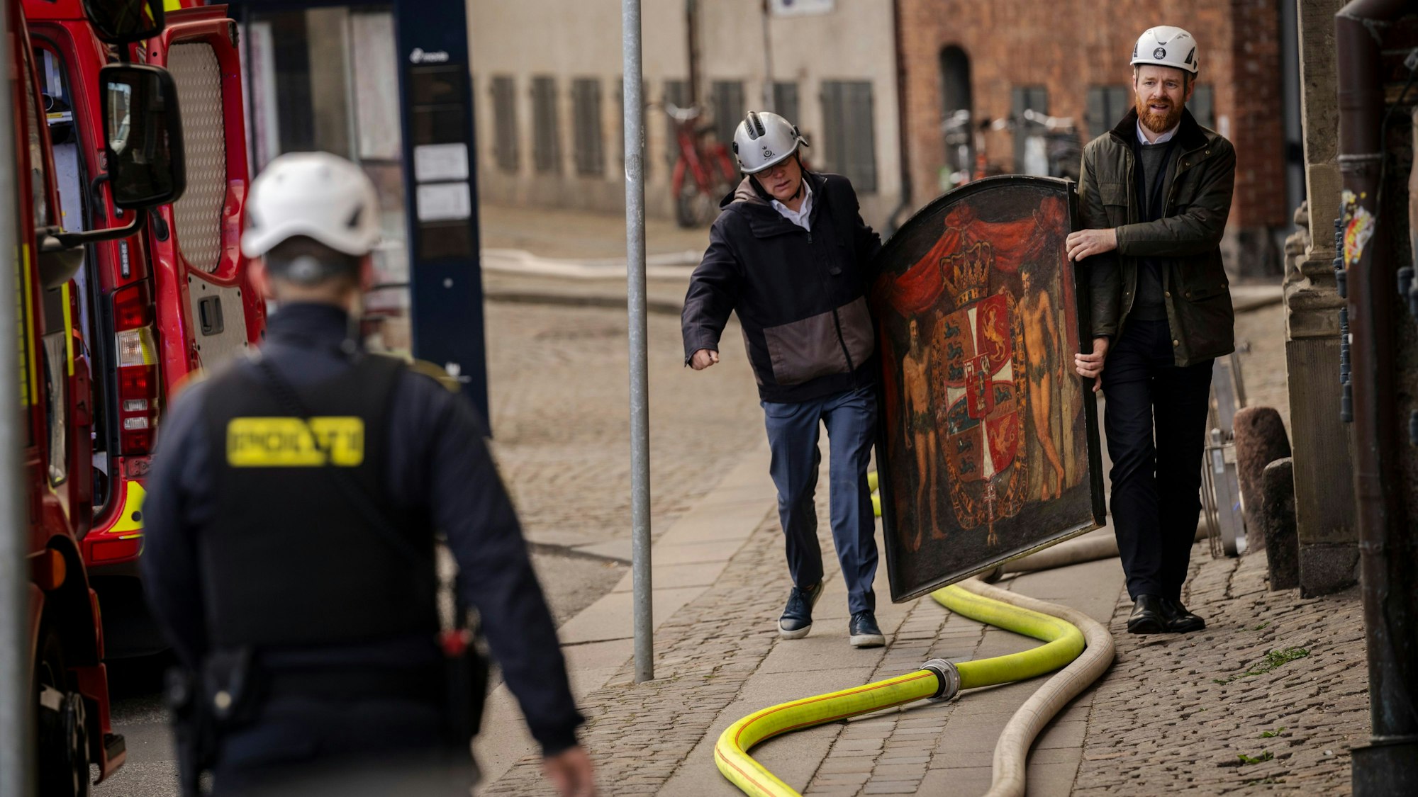 dpatopbilder - 17.04.2021, Dänemark, Kopenhagen: Der Geschäftsführer von Danish Business, Brian Mikkelsen, und der CFO von Danish Business, Philip Werner Willerslev-Olsen, tragen historische Gemälde aus dem brennenden Gebäude, während die Alte Börse ("Boersen") brennt. Eines der ältesten Gebäude Kopenhagens steht in Flammen, und seine ikonische Turmspitze ist eingestürzt. Das Dach der alten Börse (Boersen) aus dem 17. Jahrhundert, die einst das Finanzzentrum Dänemarks war, wurde am Dienstag von Flammen zerstört. Foto: Ida Marie Odgaard/Ritzau Scanpix Foto/AP +++ dpa-Bildfunk +++
