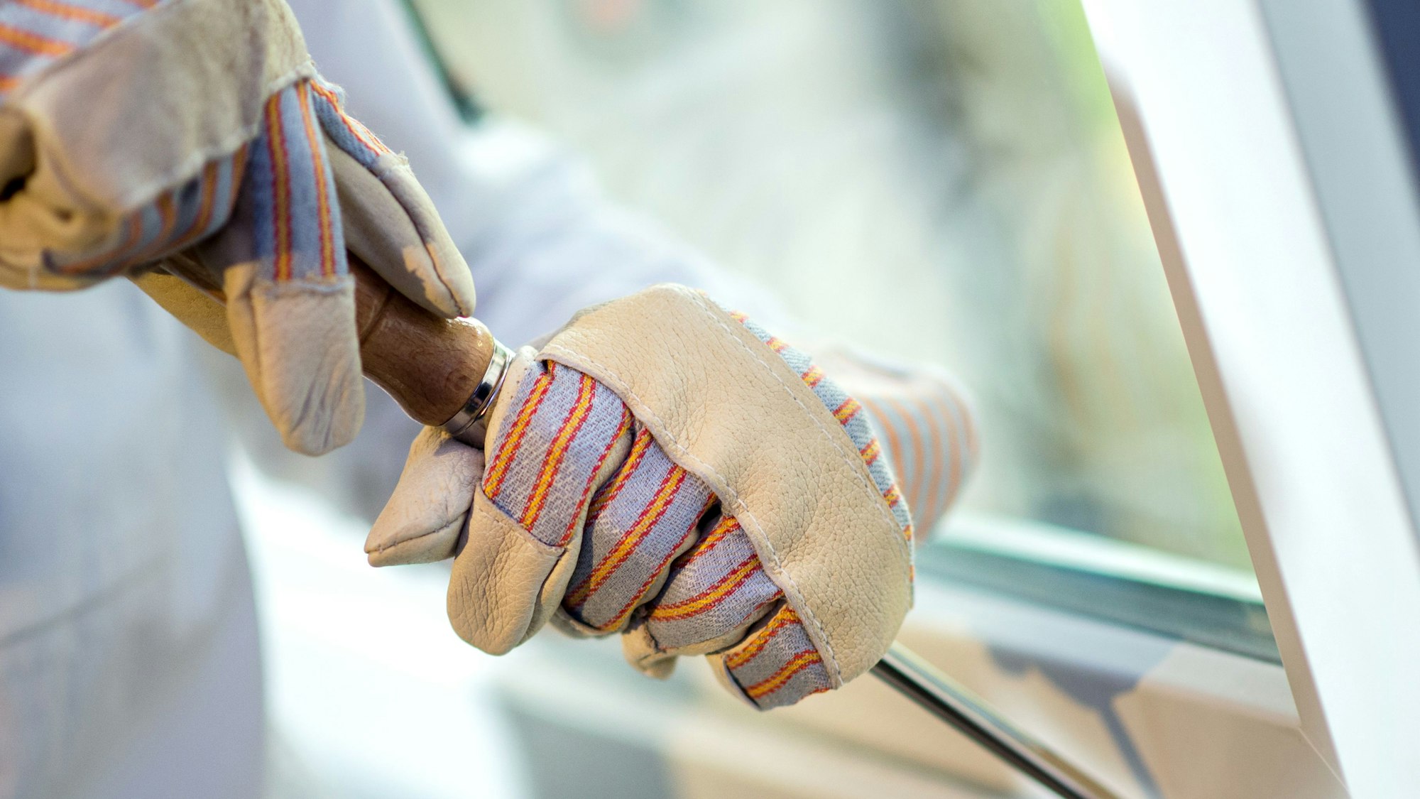 Zwei Hände in Handschuhen hebeln ein Fenster auf.