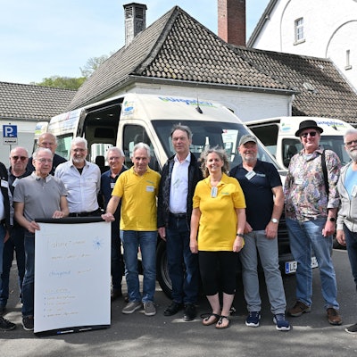 Viele Menschen stehen vor einem Kleinbus.