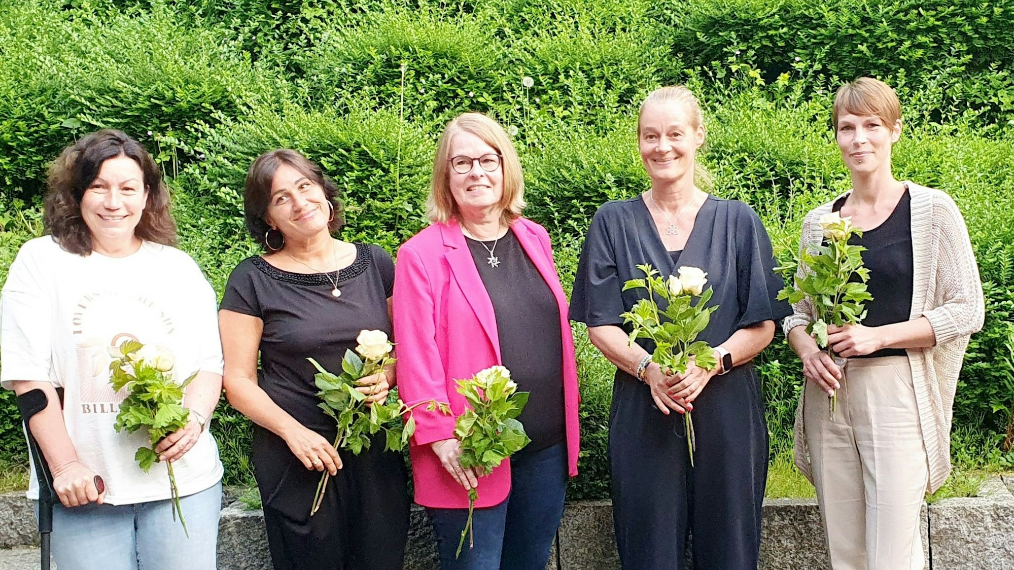 Nebeneinander stehen die fünf Frauen mit einer Rose in der Hand.
