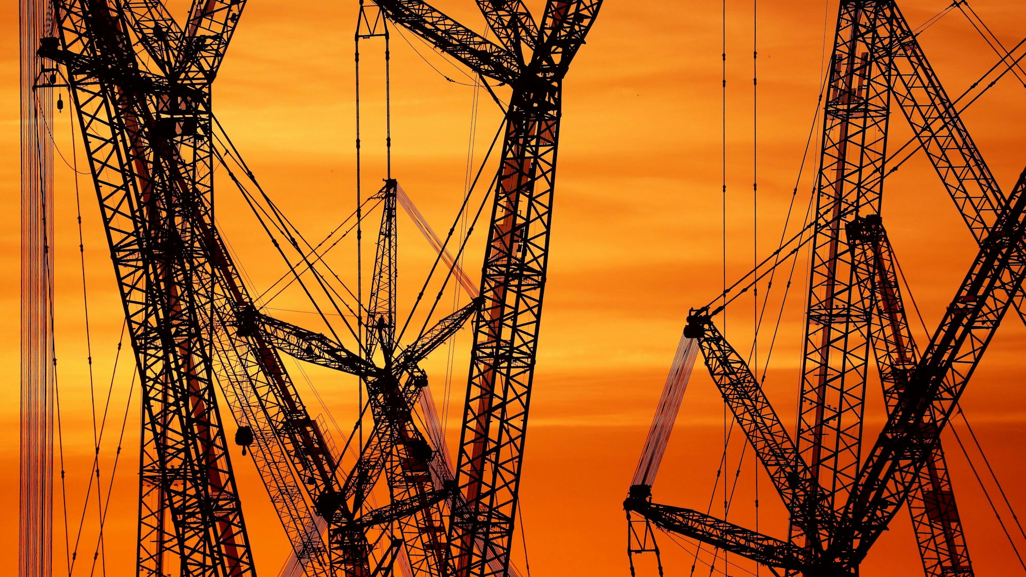 ARCHIV - 25.06.2019, Baden-Württemberg, Ehingen: Mehrere Kräne stehen auf einem Werksgelände, während im Hintergrund der Himmel von der aufgehenden Sonne rot gefärbt ist. Der Internationale Währungsfonds (IWF) hat seine Konjunkturprognose für Deutschland erneut nach unten korrigiert. Foto: Thomas Warnack/dpa +++ dpa-Bildfunk +++