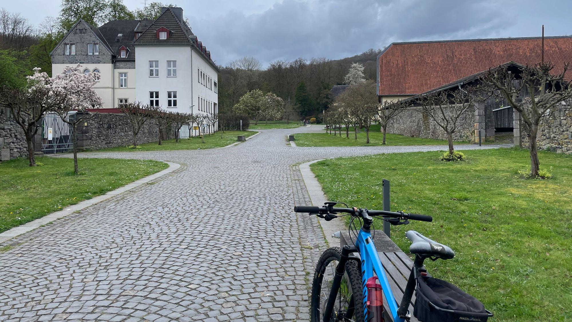 Ein Fahrrad lehnt an einer Bank, im Hintergrund ist das Kloster Heisterbach zu sehen
