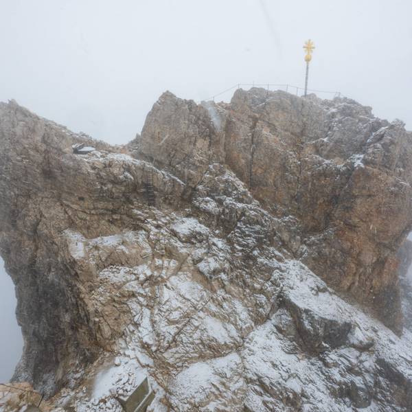 Nebelwolken umhüllen bei Schneetreiben auf der Zugspitze (2962 Meter) die verschneite Aussichtsplattform mit dem Gipfelkreuz.