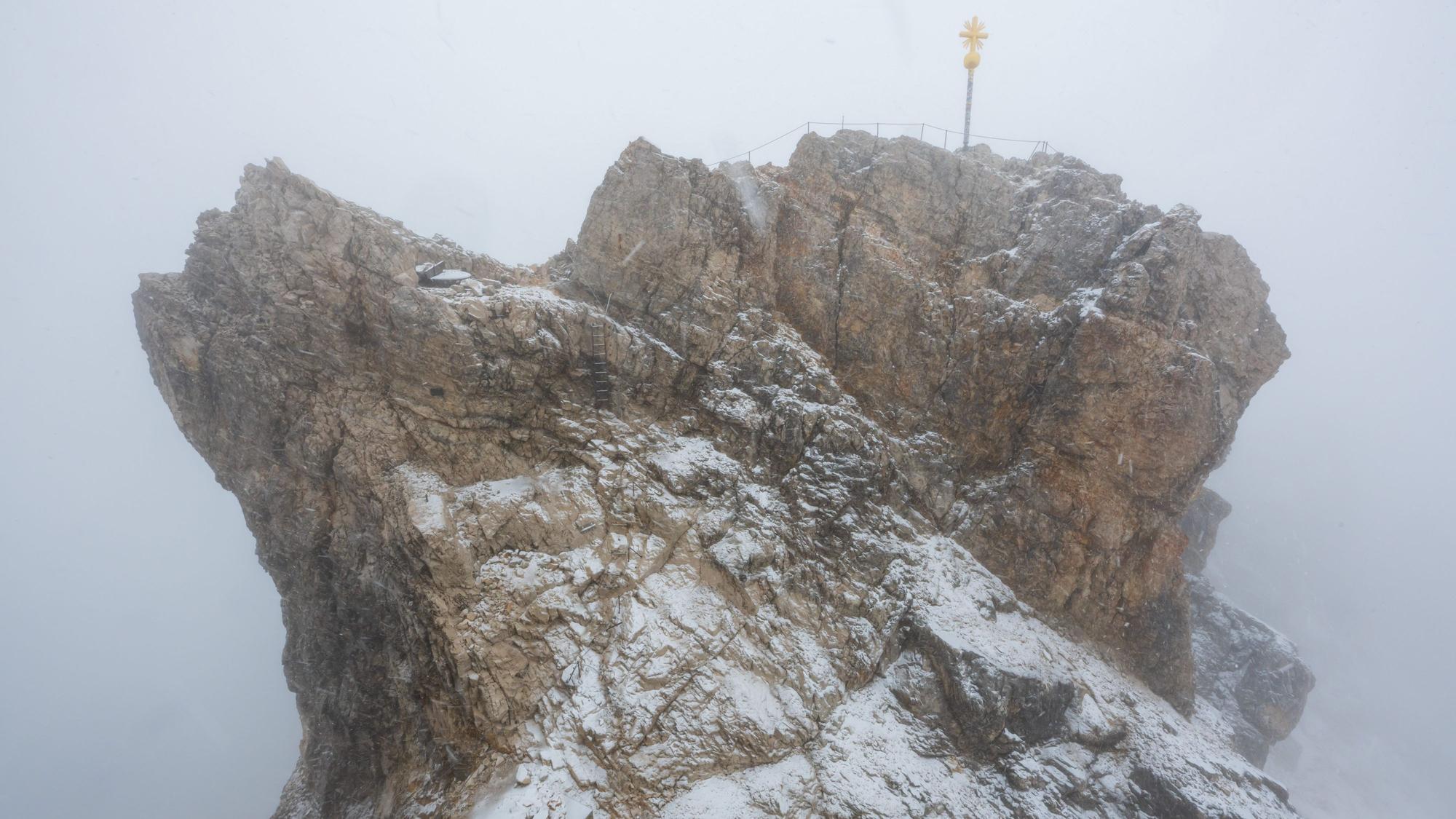 Nebelwolken umhüllen bei Schneetreiben auf der Zugspitze (2962 Meter) die verschneite Aussichtsplattform mit dem Gipfelkreuz.