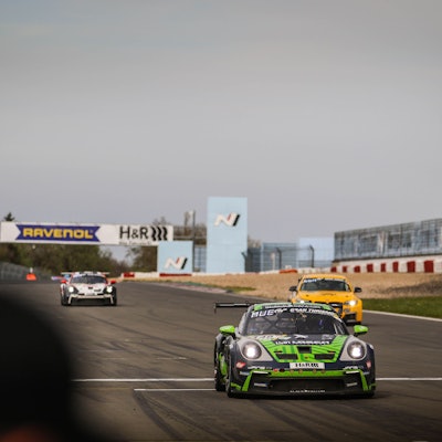 Tobias Müller überquert in seinem Porsche die Ziellinie, am Rand wird die schwarz-weiß-karierte Flagge geschwenkt.