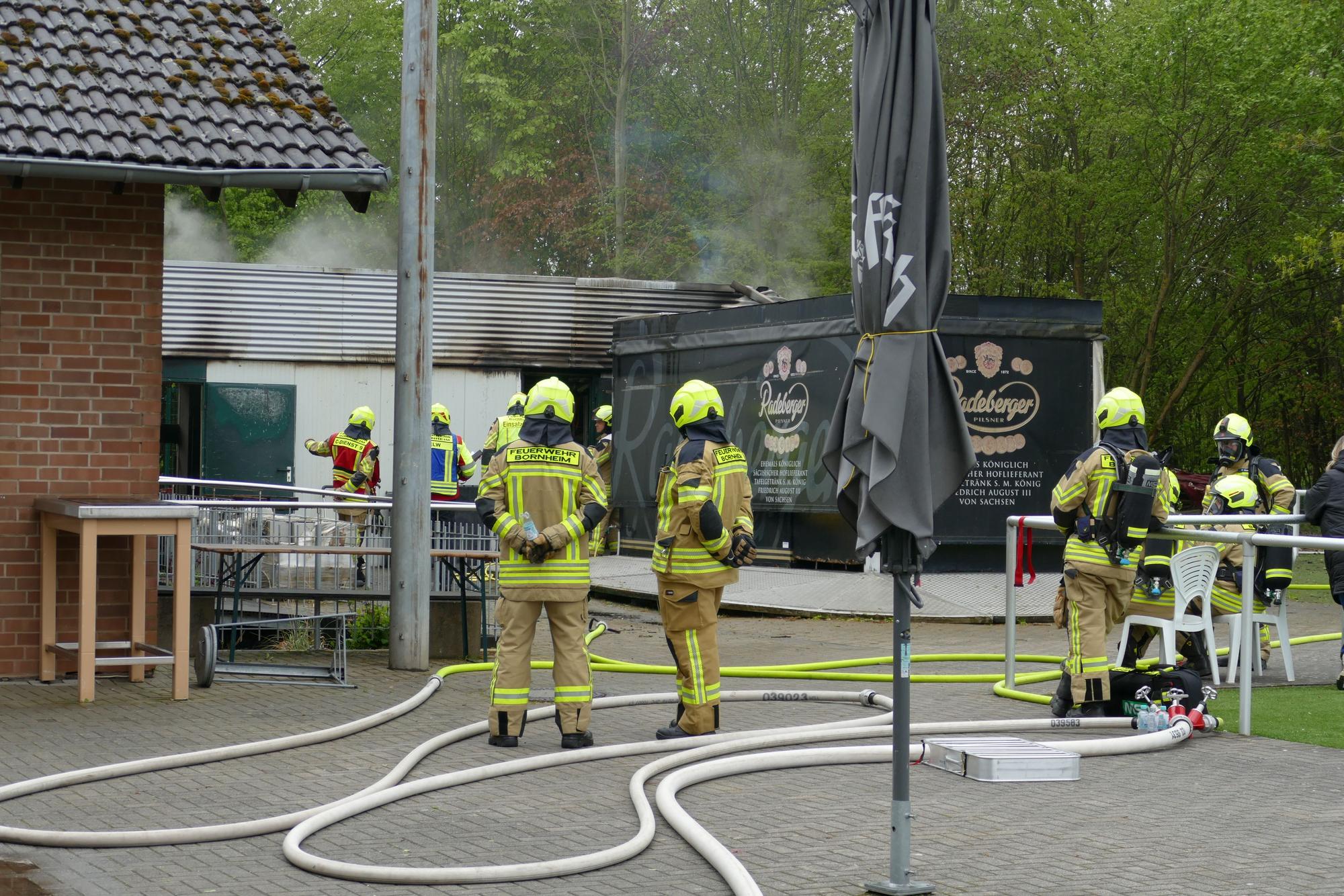 Feuerwehrleute auf einem Sportplatzgelände, im Hintergrund qualmt es.