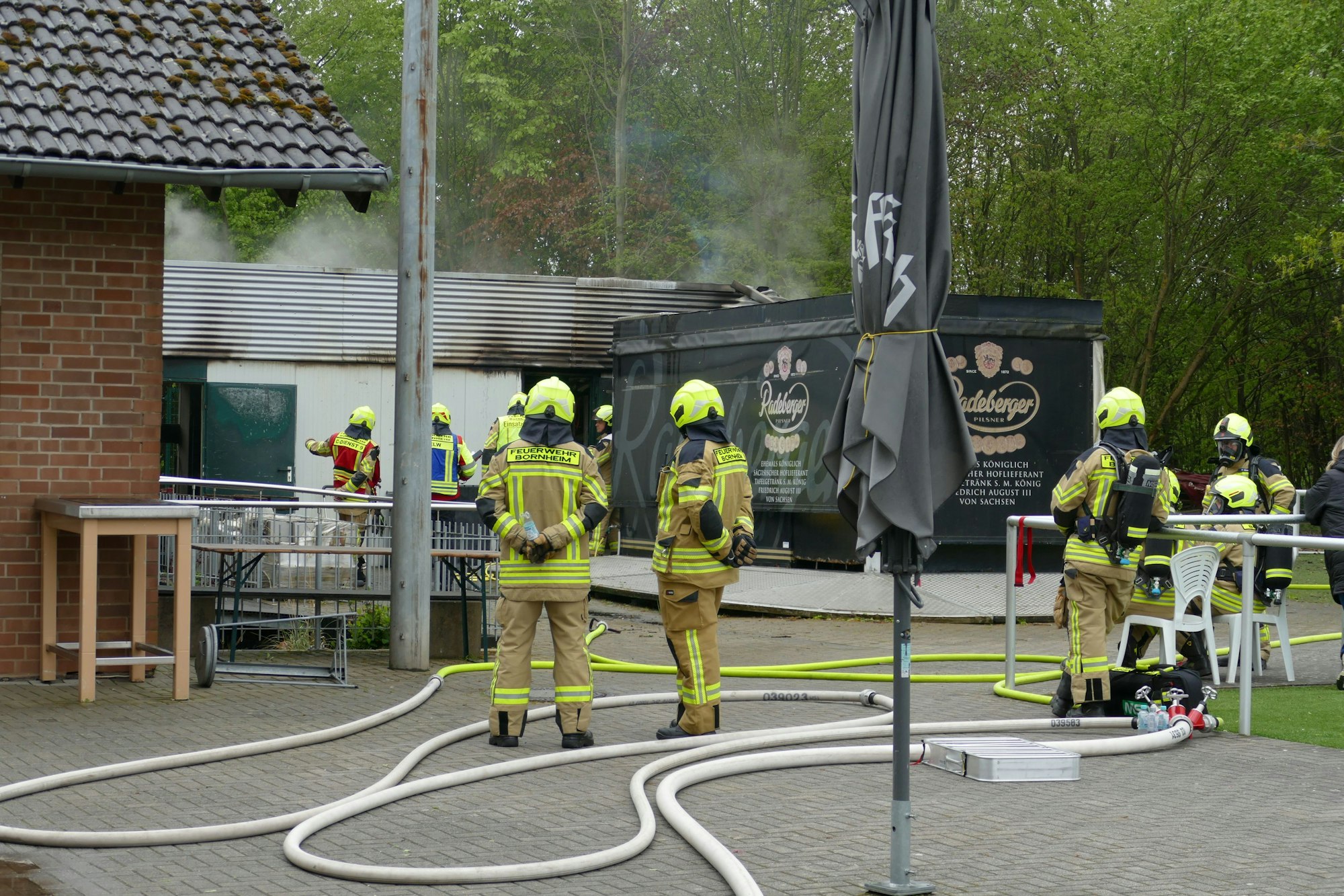 Feuerwehrleute auf einem Sportplatzgelände, im Hintergrund qualmt es.