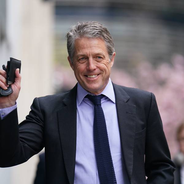Hugh Grant lächelt und winkt.