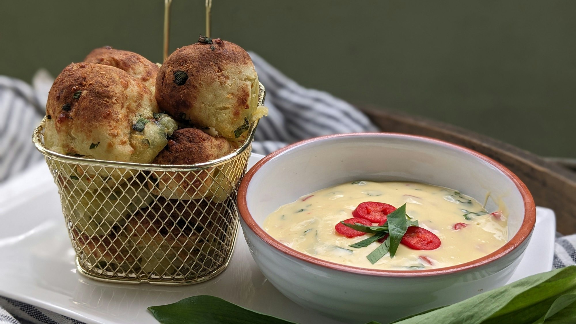 Kartoffel-Bärlauch-Bällchen stehen in einem Körbchen neben einer Schüssel mit Sauce Hollandaise-Dip.