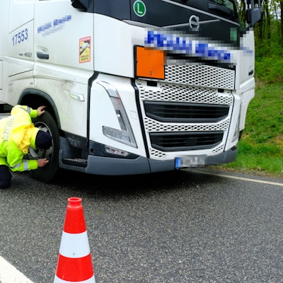Ein Polizeibeamter in signalgelber Kleidung überprüft die Bremsanlage eines Lastwagens.