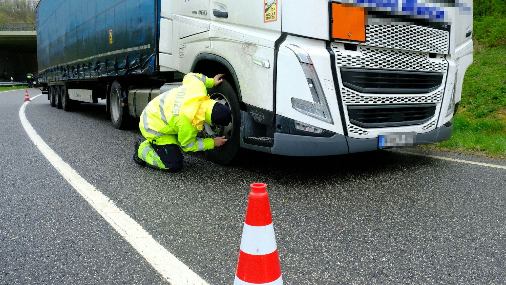 Ein Polizeibeamter in signalgelber Kleidung überprüft die Bremsanlage eines Lastwagens.