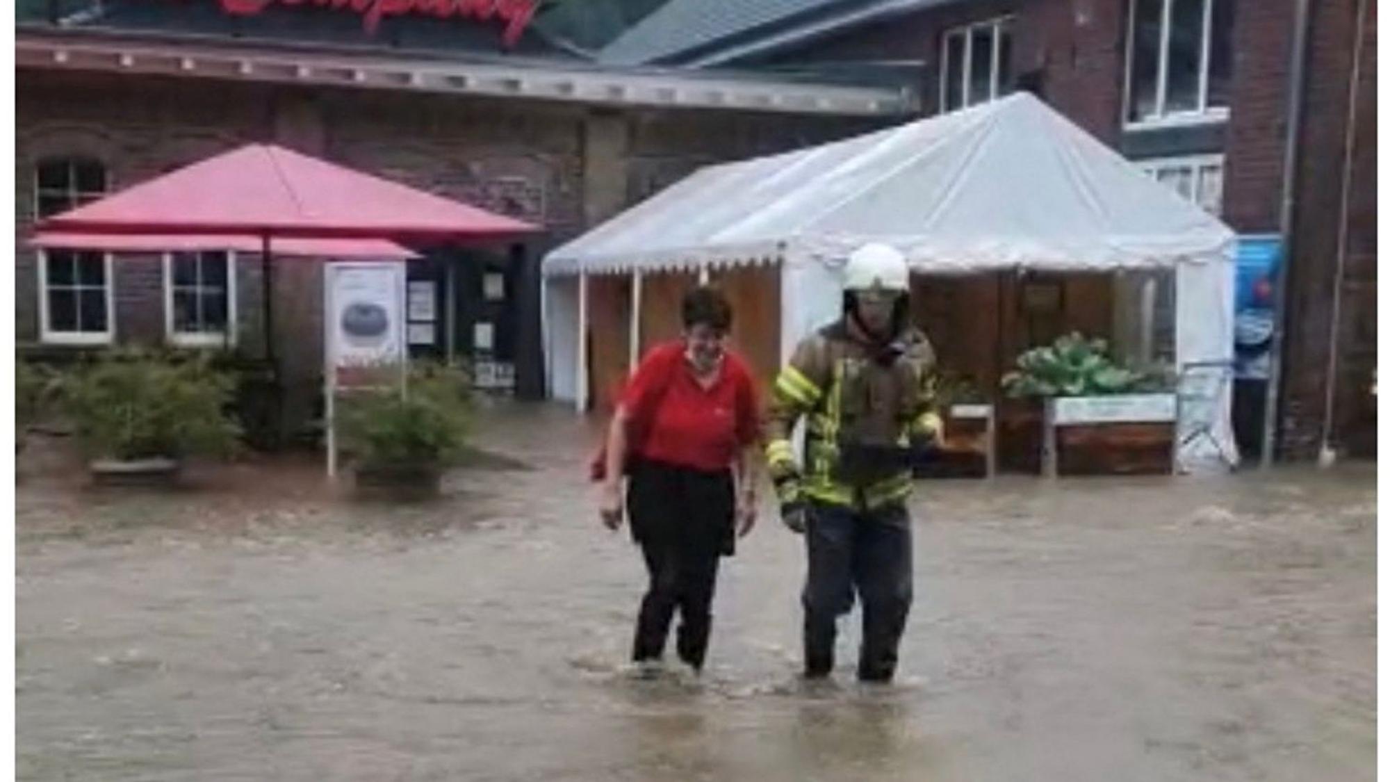 Die Angestellte und ein Feuerwehrmann waten knietief durch das Wasser.