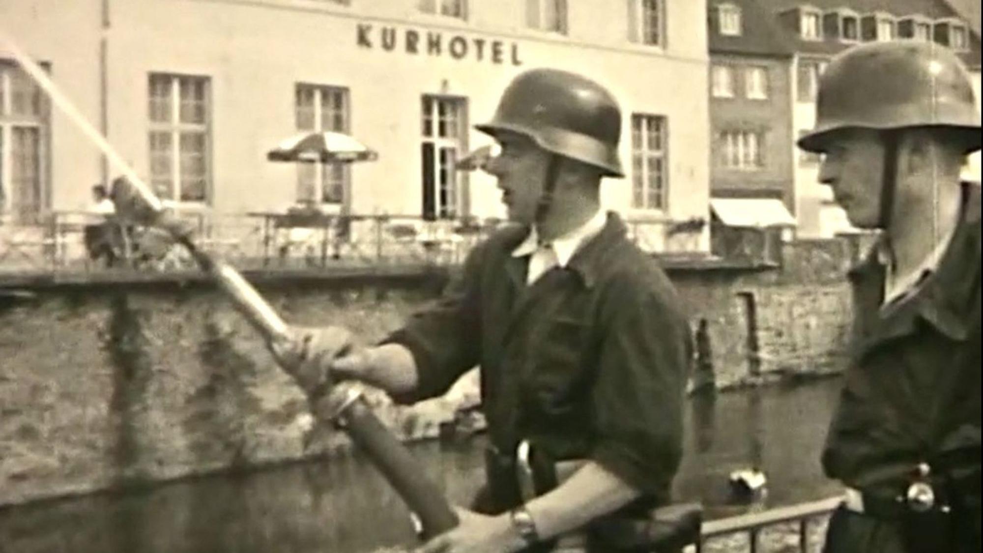Zwei Feuerwehrleute stehen vor dem ehemaligen Kurhotel, einer hält einen Schlauch.