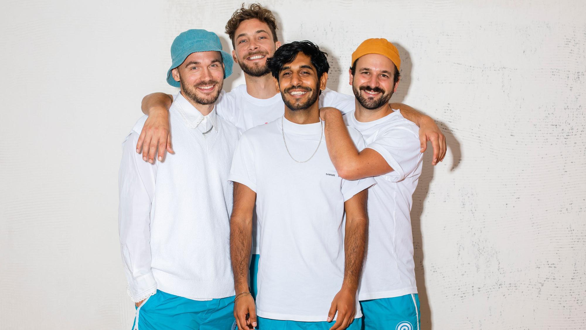 Die vier Bandmitglieder stehen zusammen und grinsen in die Kamera.