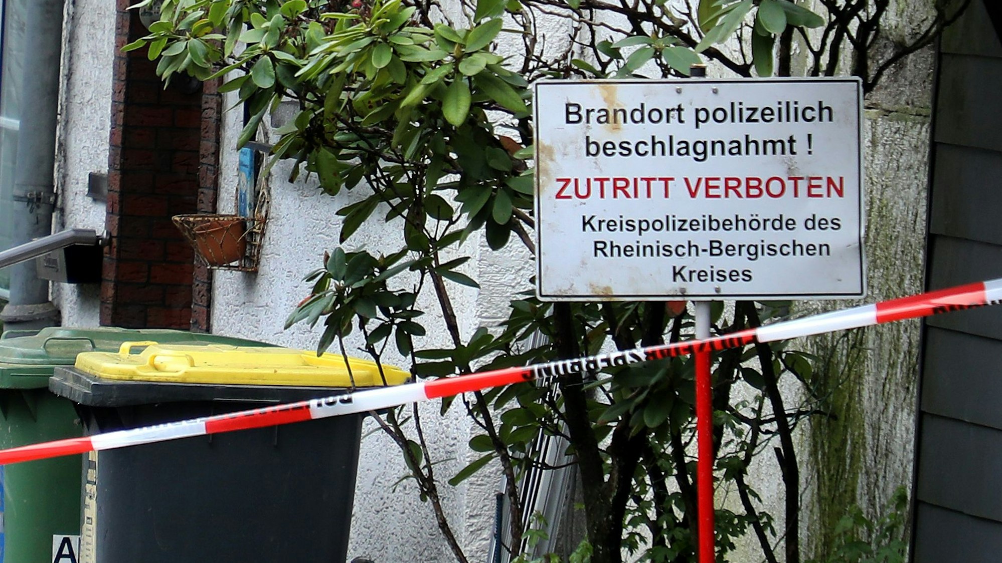 Vor einem Haus steht ein Schild mit der Aufschrift „Brandort polizeilich beschlagnahmt! Zutritt verboten“. Davor ist Polizei-Absperrband zu sehen.