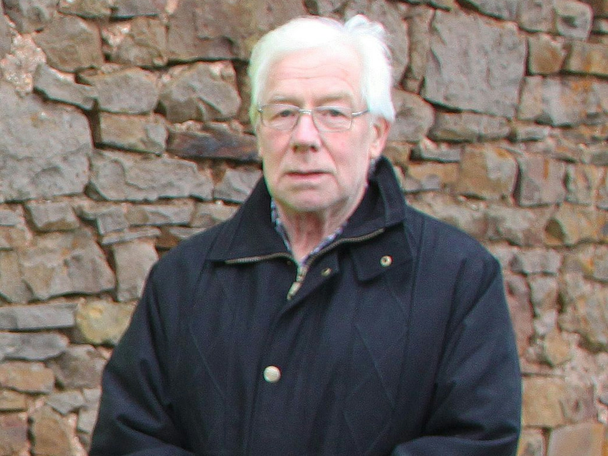 Das Bild zeigt den Ortsvorsteher vor einer Bruchsteinmauer.