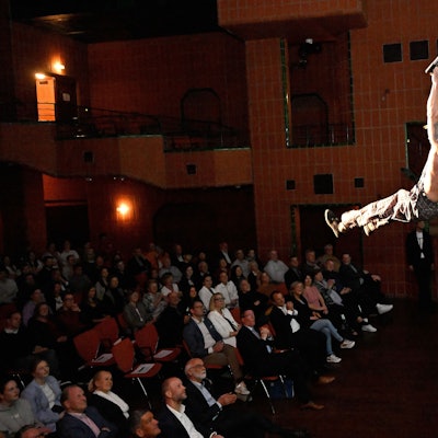 Ein Mann hängt an einer Laterne über dem Publikum im großen Saal des Bergischen Löwen.