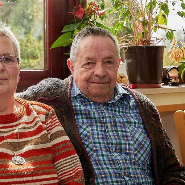 Helene und Klaus Berends sitzen vor einem Fenster, er hat seinen Arm um sie gelegt.