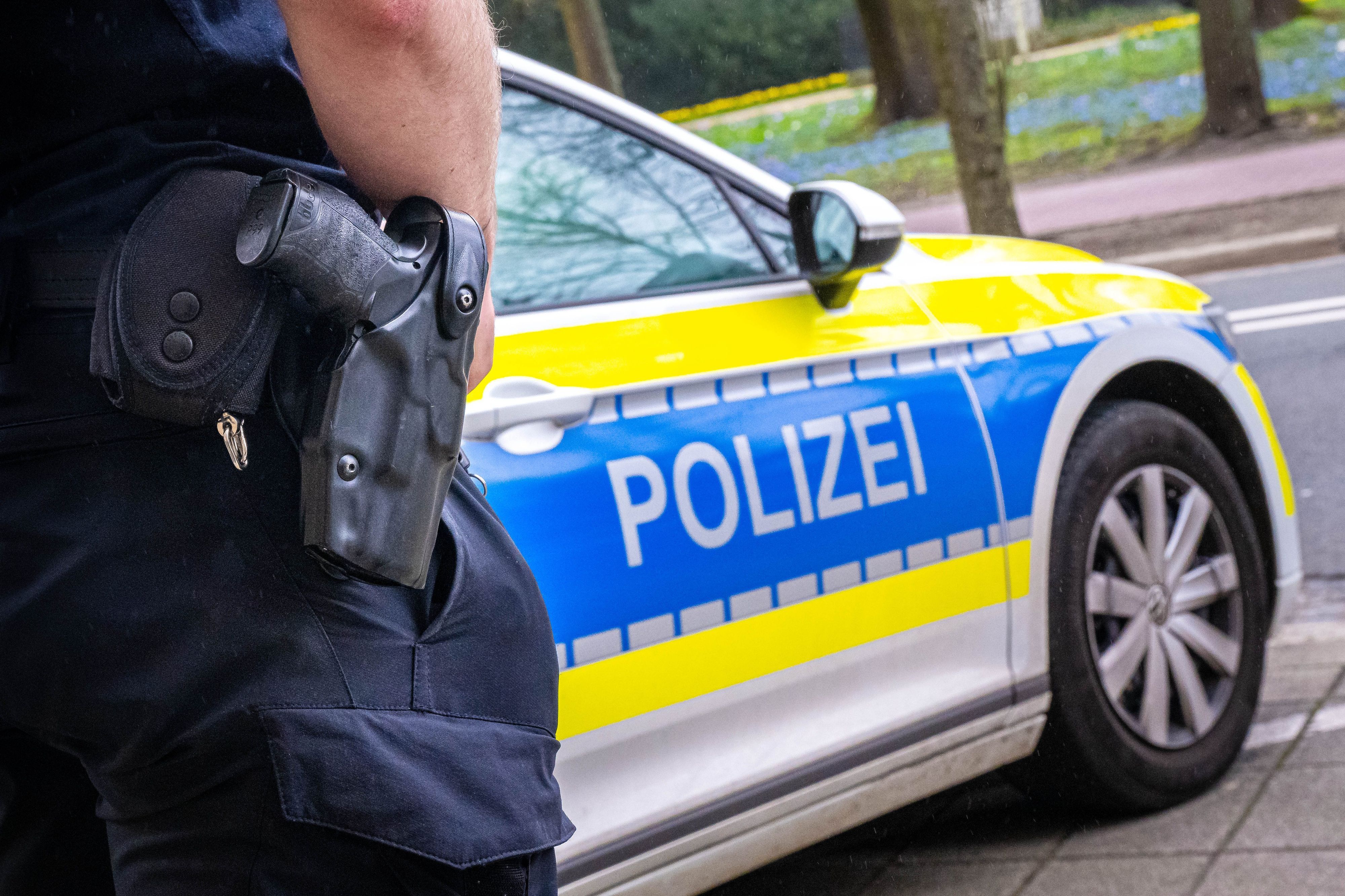 Auf dem Foto ist ein Polizist zu sehen, der vor einem Streifenwagen steht.