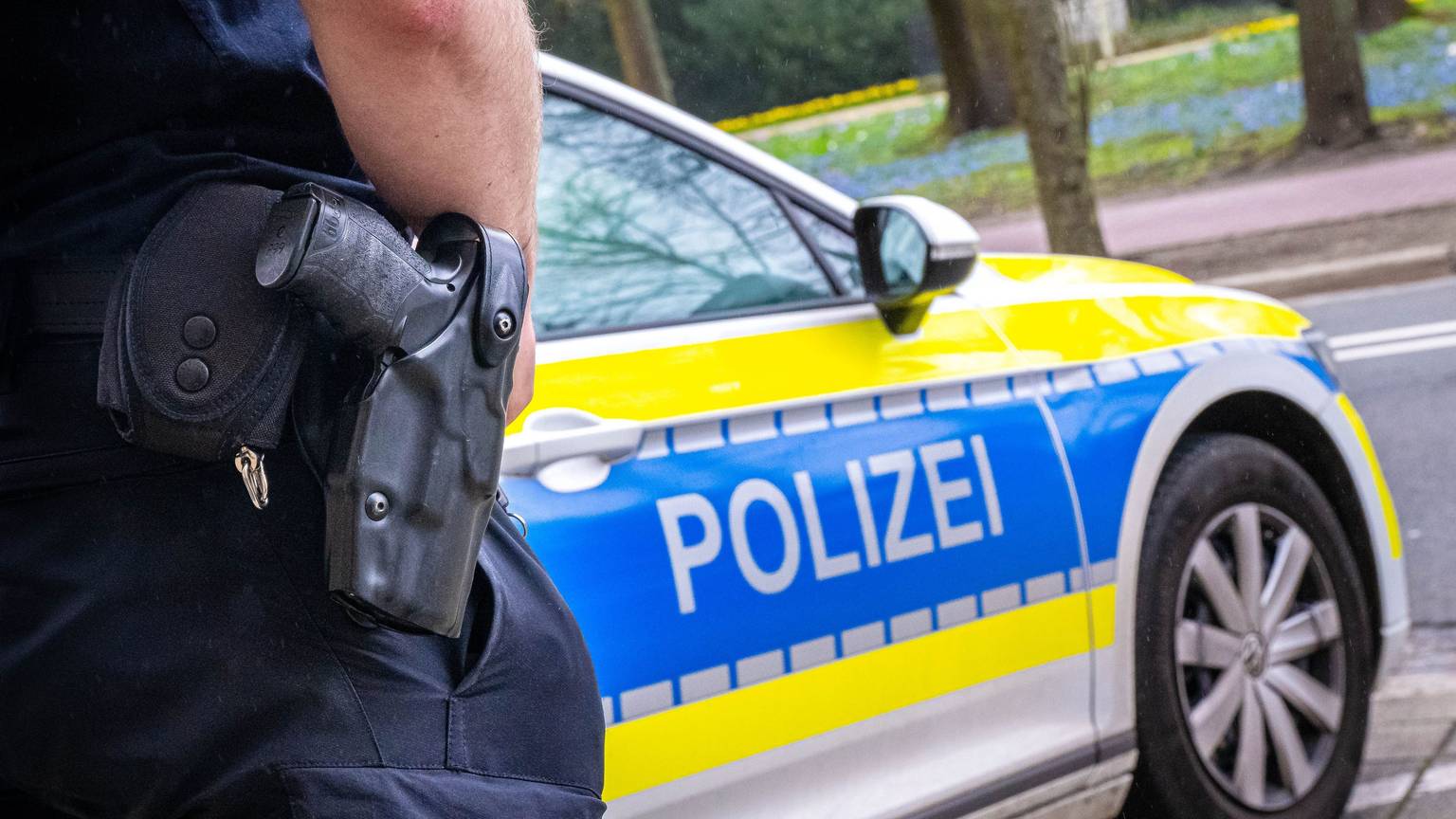 Auf dem Foto ist ein Polizist zu sehen, der vor einem Streifenwagen steht.