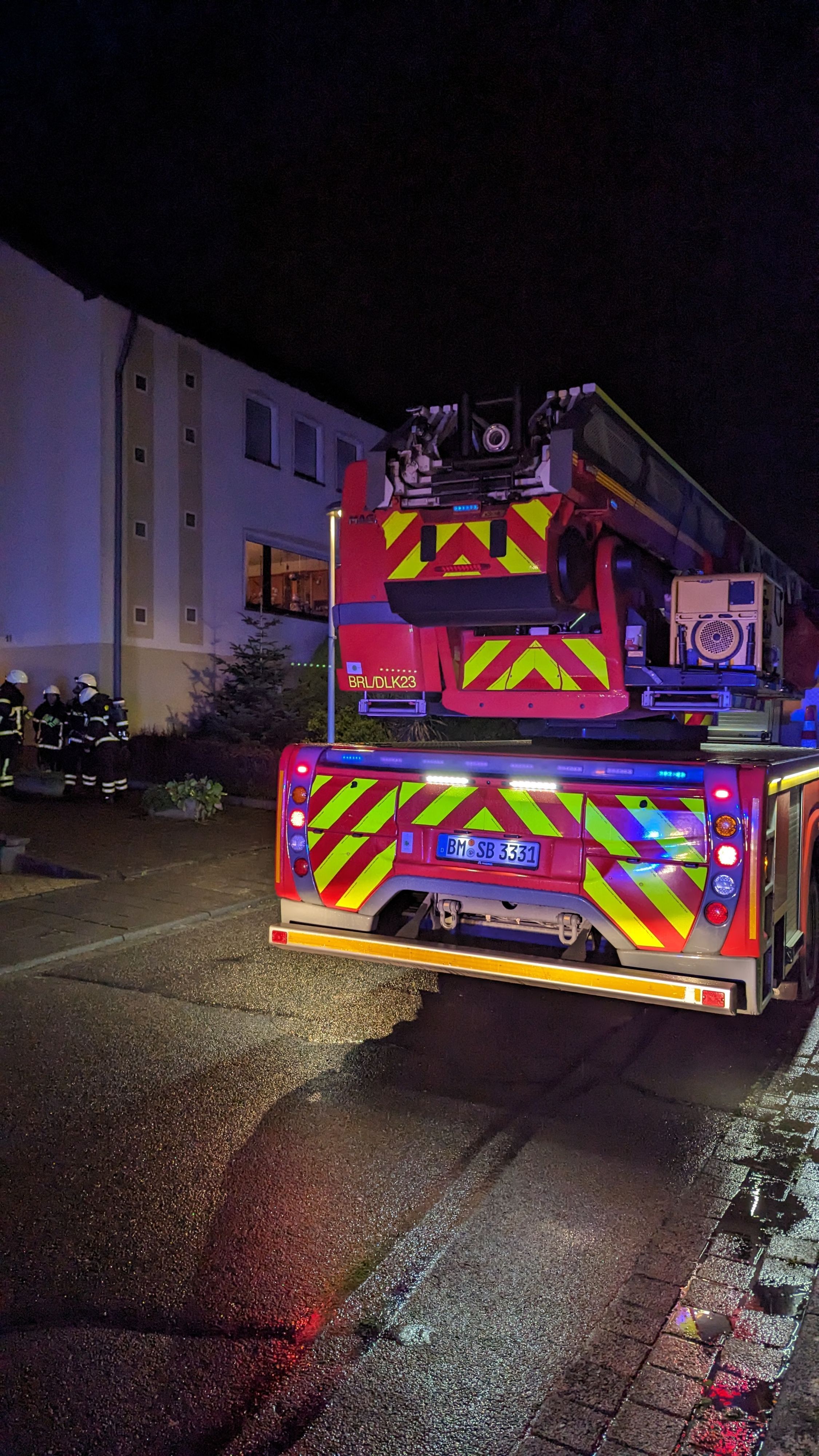 Ein Feuerwehreinsatzfahrzeug. Im Hintergrund Einsatzkräfte und ein Mietshaus.