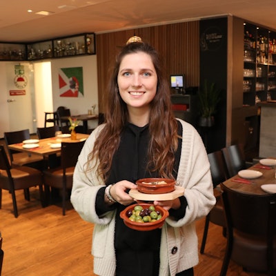Eine junge Frau steht mit einigen Schalen mit Tapas in den Händen im Gastraum.