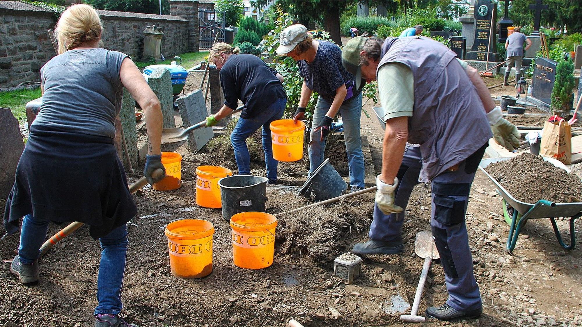 Frauen und Männer befreien den Bad Münstereifeler Friedhof nach der Flut vom Schlamm.