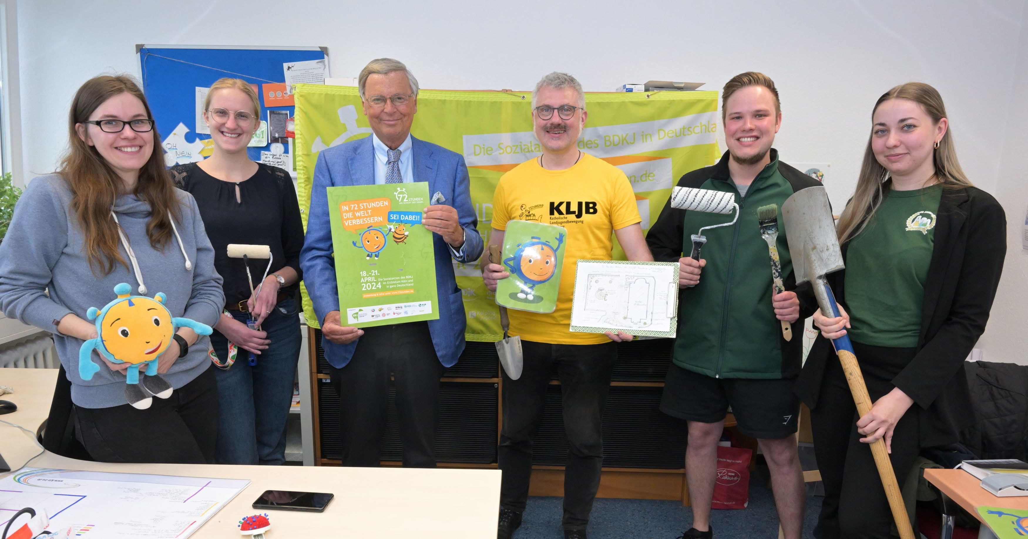 Menschen stehen mit Spaten, Plakat und anderen Utensilien beim Pressetermin zur 72-Stunden-Aktion des BDKJ in der Katholischen Jugendagentur in Bergisch Gladbach.