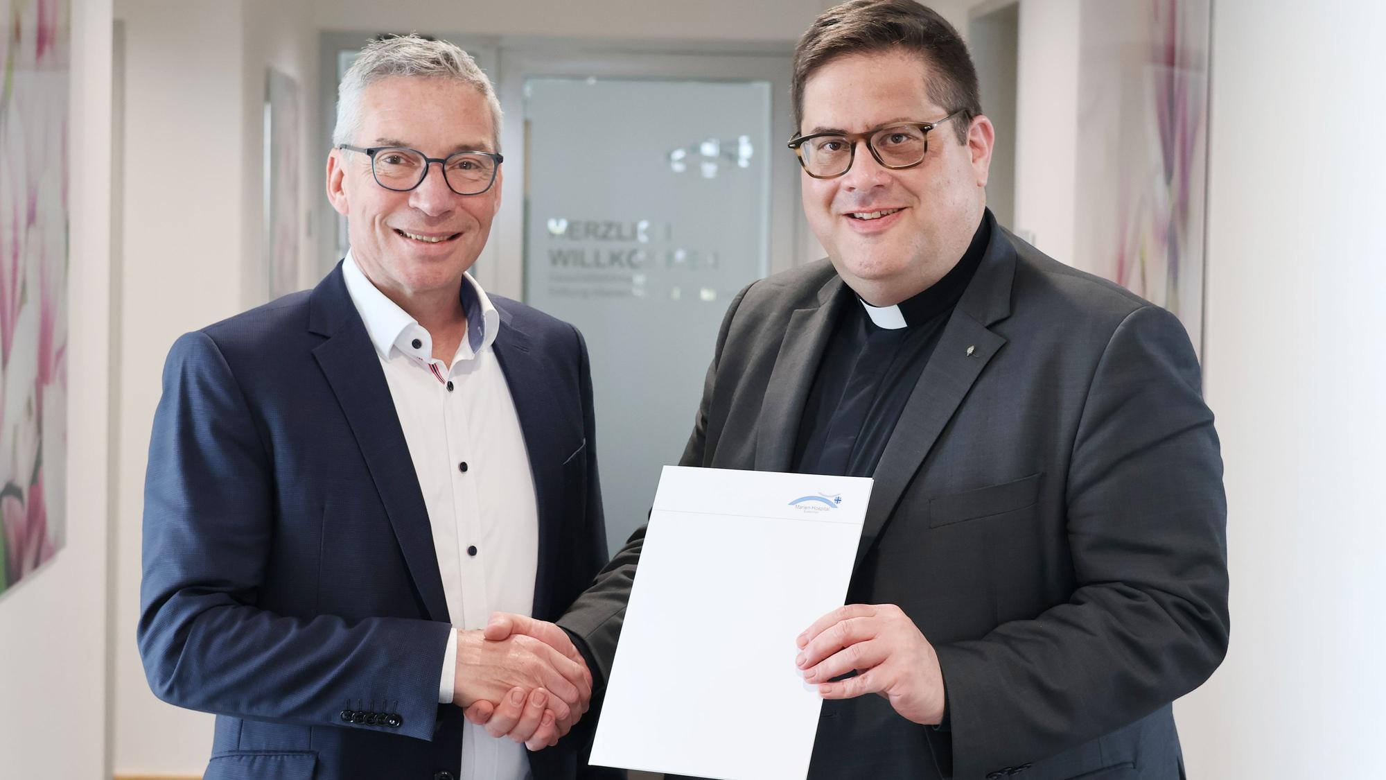 Das Bild zeigt Schneider und Hopmann, wie sie sich die Hand geben und die Zusammenarbeit so besiegeln.
