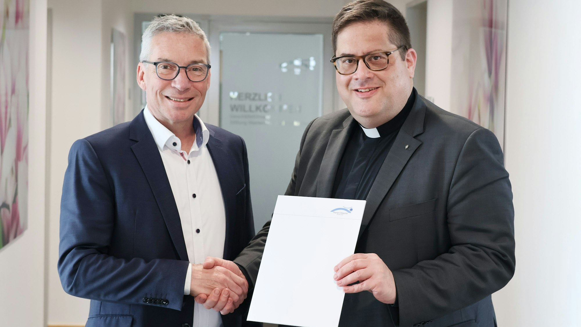 Das Bild zeigt Schneider und Hopmann, wie sie sich die Hand geben und die Zusammenarbeit so besiegeln.