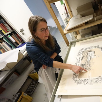 Eine Frau zeigt auf ein historisches Plakat aus dem 19. Jahrhundert.