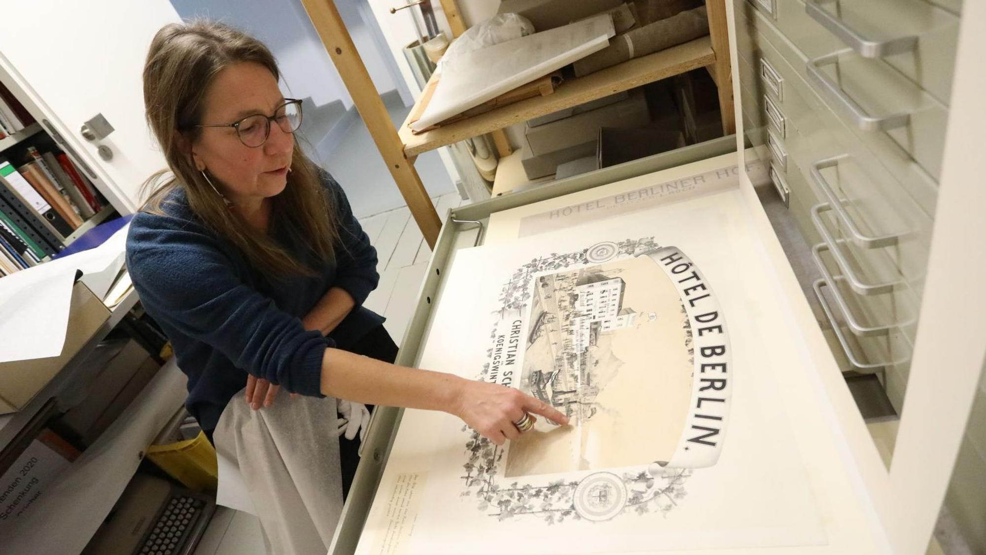 Eine Frau zeigt auf ein historisches Plakat aus dem 19. Jahrhundert.