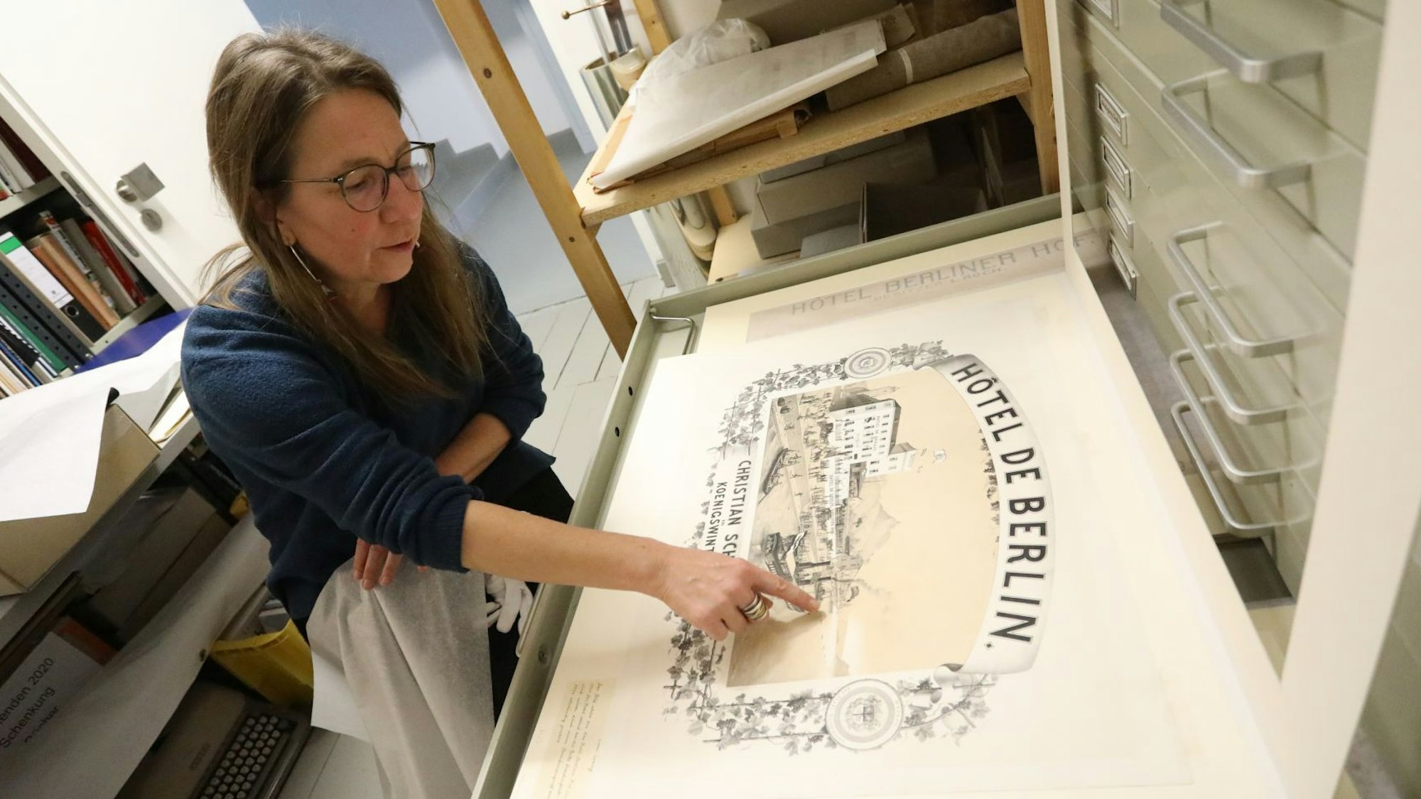 Eine Frau zeigt auf ein historisches Plakat aus dem 19. Jahrhundert.