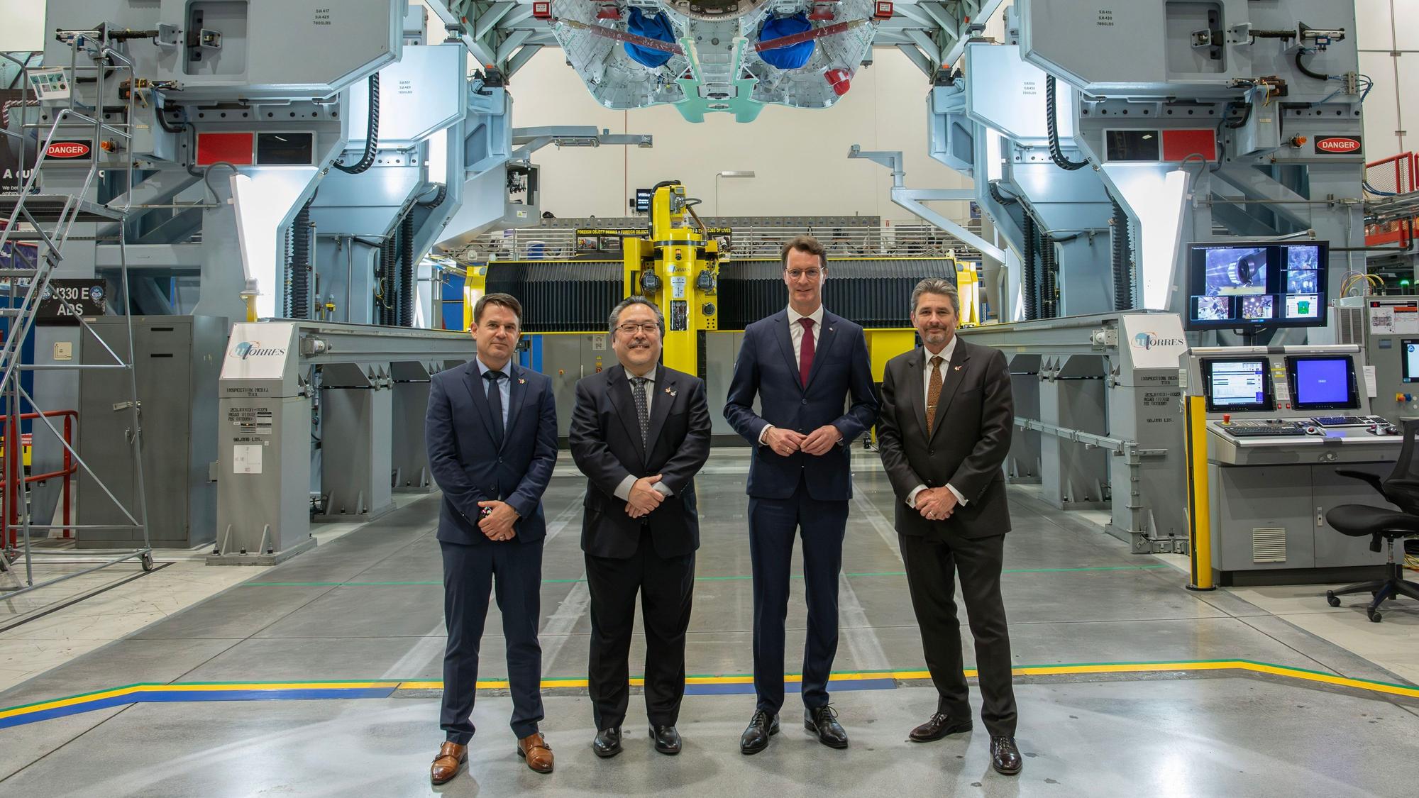 Palmdale: Mike Schmidt (l-r, CEO Rheinmetall Aviation Services GmbH), Glenn Masukawa (Vice President and F-35 Program Manager), Hendrik Wüst (CDU), Ministerpräsident des Landes Nordrhein-Westfalen) und Tom Jones (Corporate Vice President & Sector President, Aeronautics Systems) stehen bei einem Besuch des Produktionswerks des Rüstungsunternehmens Northrop Grumman in einer Halle.