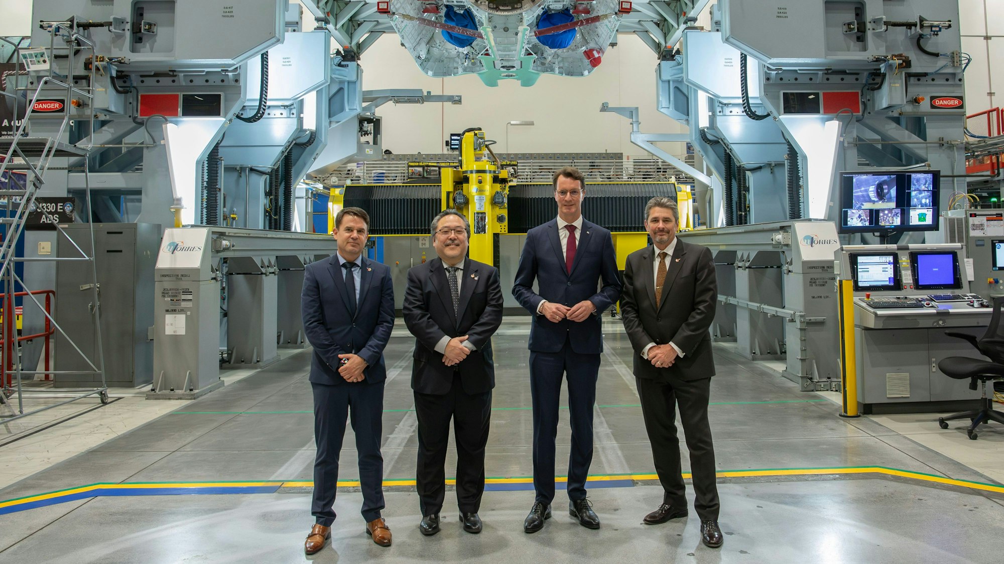 Palmdale: Mike Schmidt (l-r, CEO Rheinmetall Aviation Services GmbH), Glenn Masukawa (Vice President and F-35 Program Manager), Hendrik Wüst (CDU), Ministerpräsident des Landes Nordrhein-Westfalen) und Tom Jones (Corporate Vice President & Sector President, Aeronautics Systems) stehen bei einem Besuch des Produktionswerks des Rüstungsunternehmens Northrop Grumman in einer Halle.