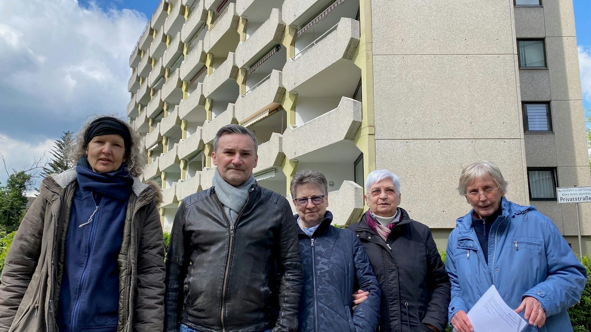 Zu sehen ist eine Gruppe von Menschen vor einem mehrgeschossigen Gebäude.