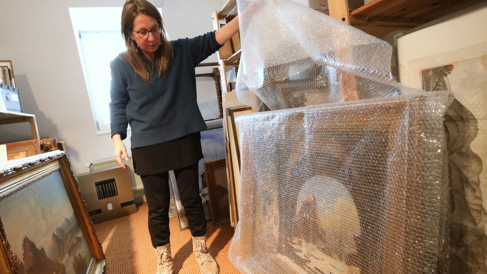 Eine Frau hebt eine Plastikplane an, die ein großes Ölgemälde schützt.