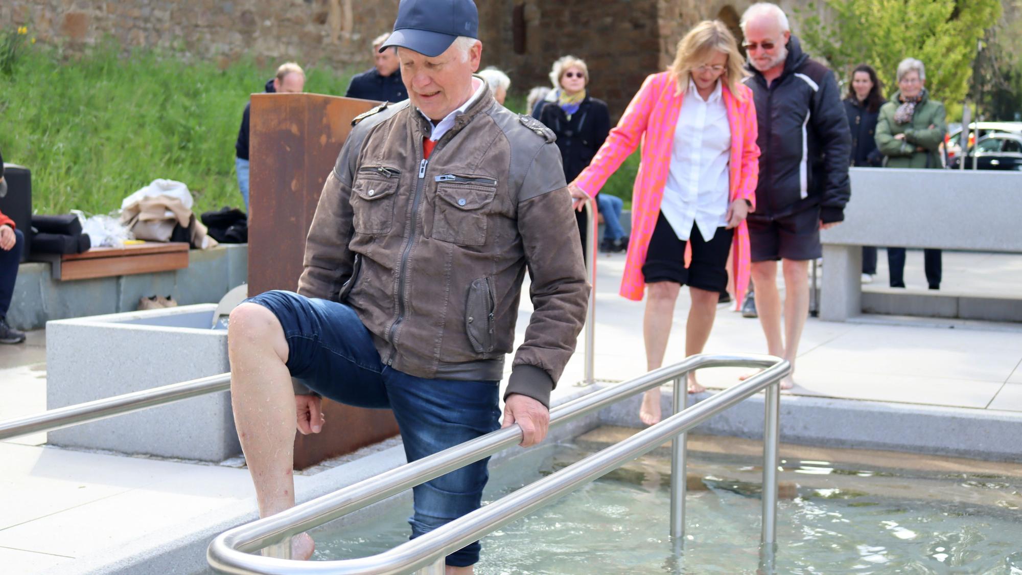 Ein Mann stakst mit hochgekrempelter Hose durch ein Kneipp-Wassertretbecken.