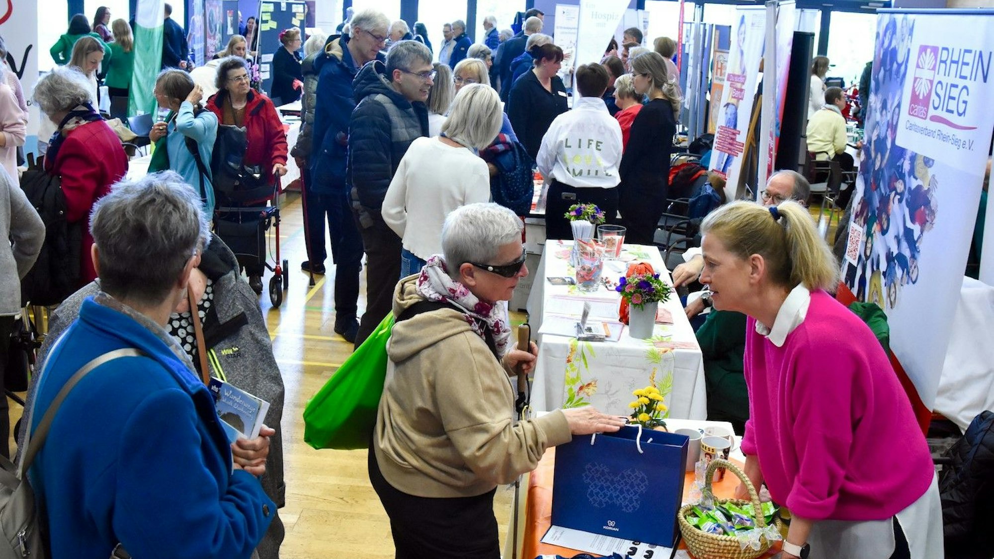 Menschen bei einer Messe in einer Veranstaltungshalle. im Vordergrund sind zwei Frauen im Gespräch.